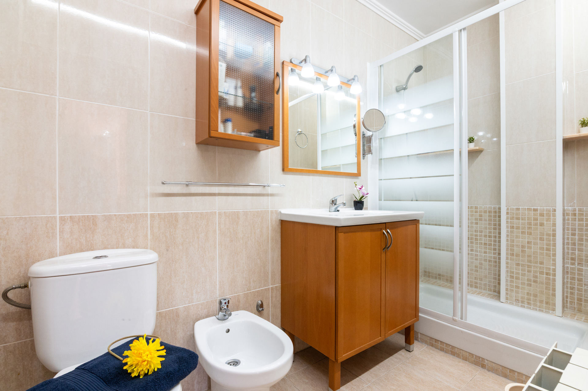 Fotografía inmobiliaria editada de baño moderno con ducha, sanitarios y muebles de madera. Imagen optimizada con corrección de color, iluminación profesional y enfoque en el detalle arquitectónico.
