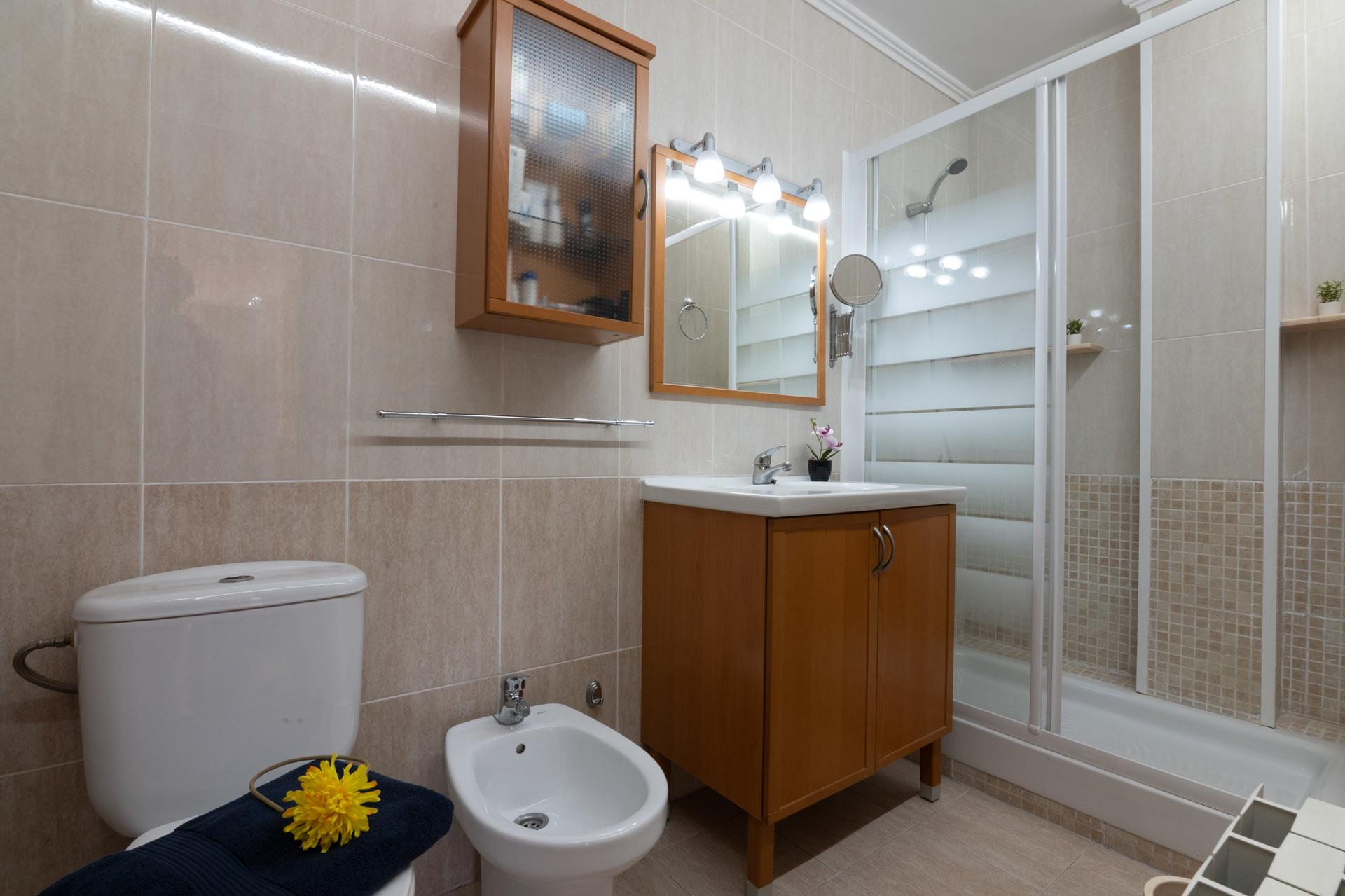 Fotografía inmobiliaria sin edición de baño completo con ducha, bidet y muebles de madera clara. Imagen profesional para venta o alquiler de propiedades.