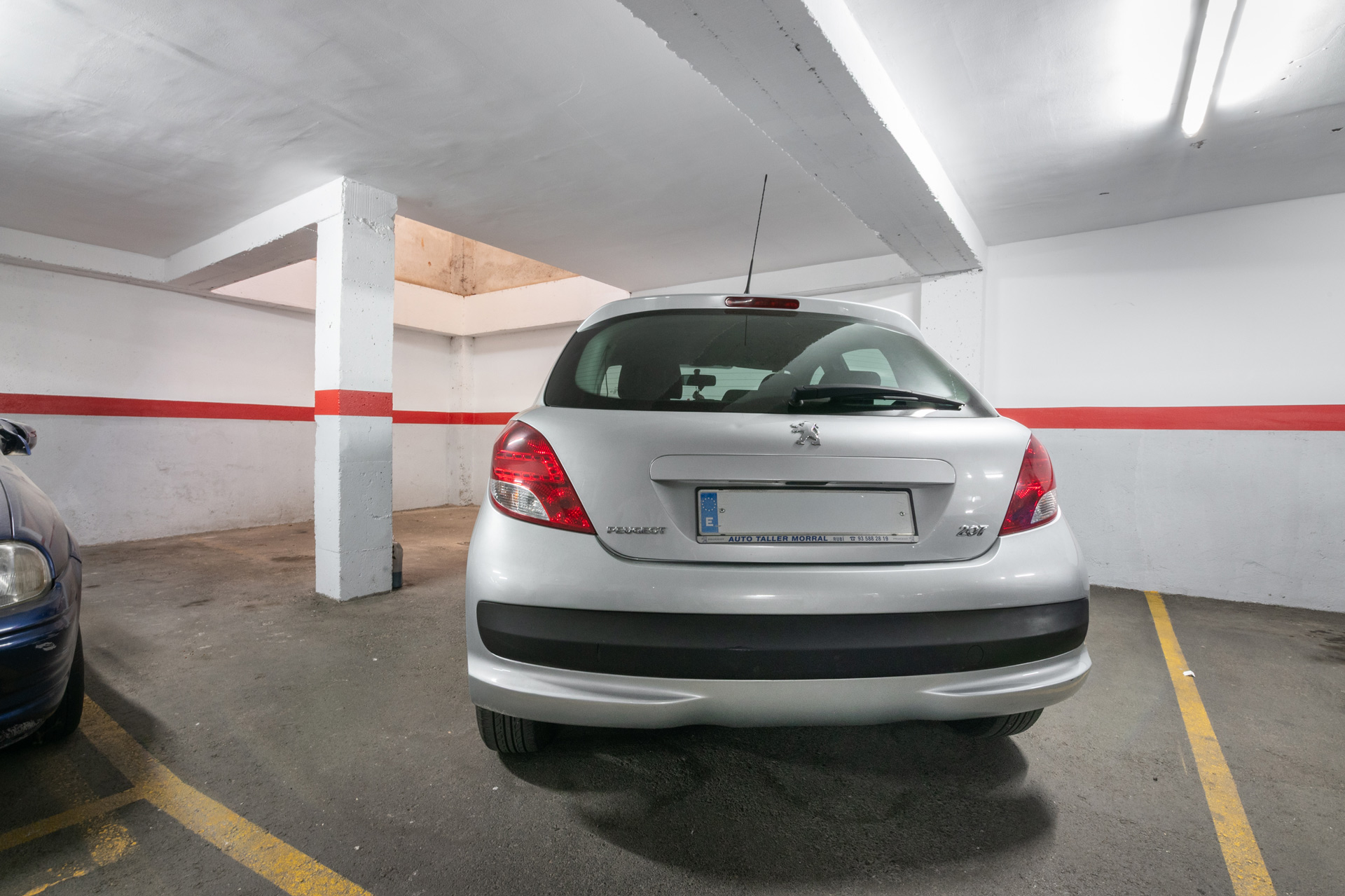 Fotografía inmobiliaria editada de garaje o plaza de aparcamiento interior, con patente censurada y corrección de iluminación. Imagen profesional para destacar el espacio en venta o alquiler.