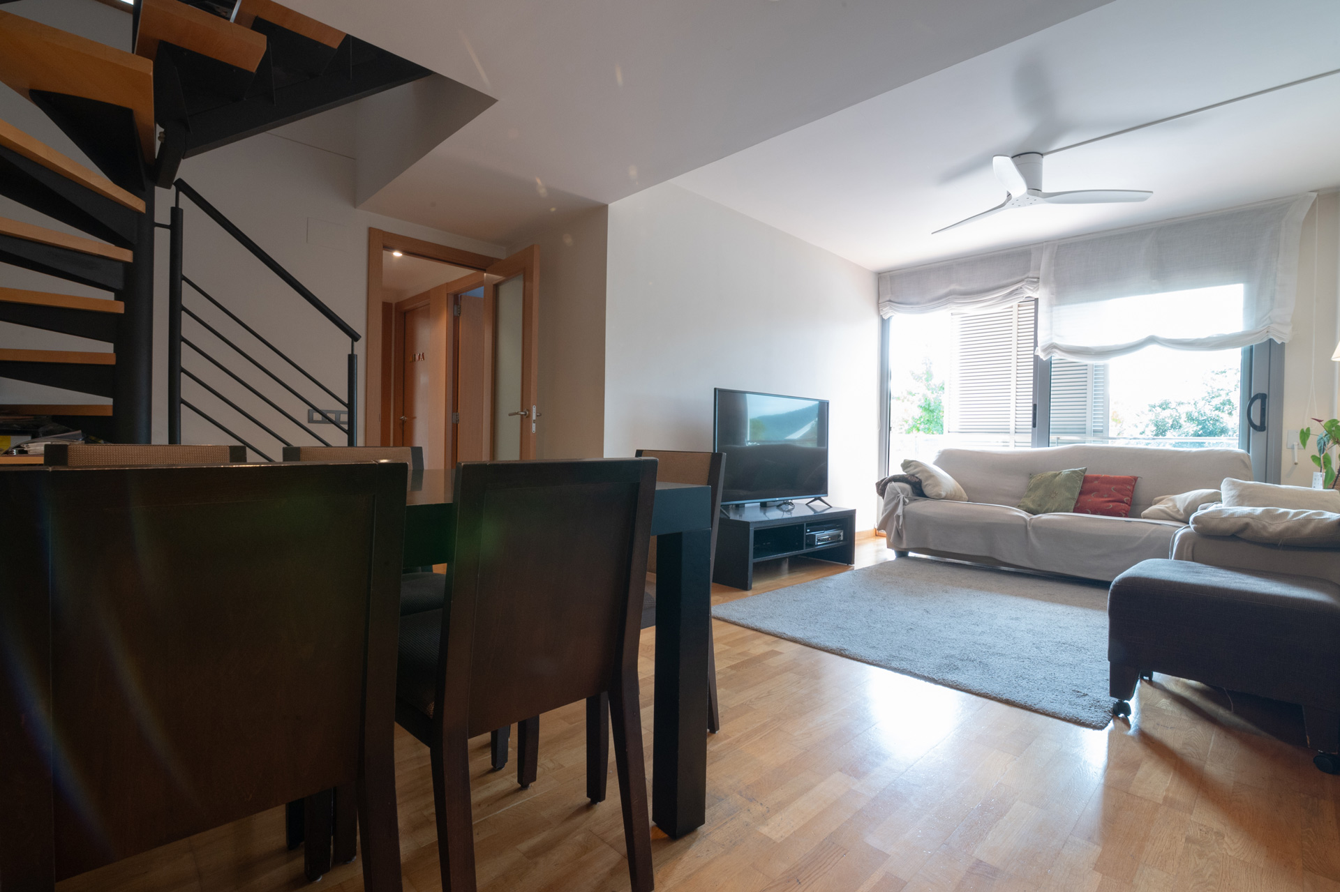 Fotografía inmobiliaria sin edición de living comedor moderno con escalera y ventanales. Imagen capturada con luz natural para mostrar la amplitud y distribución real del espacio.