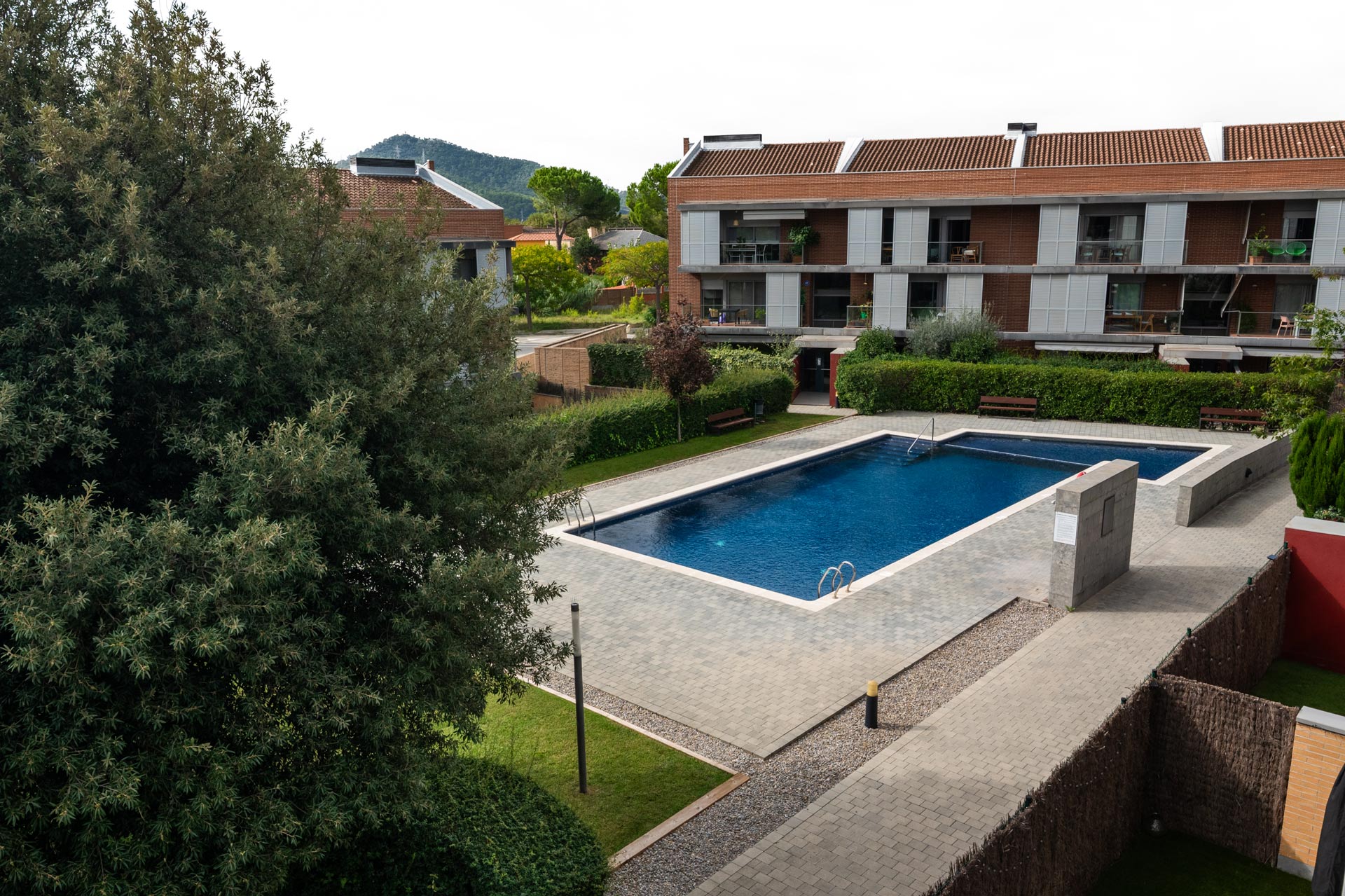 Fotografía inmobiliaria sin edición de piscina y áreas comunes en condominio moderno. Imagen profesional capturada con luz natural para mostrar los espacios exteriores reales de la propiedad.